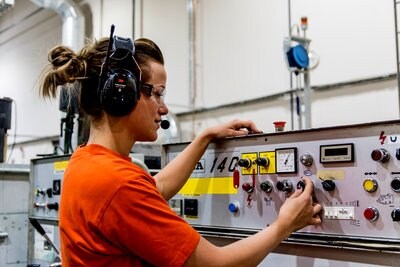 Imagen de un hombre operando en un entorno de fabricación, sosteniendo una linterna con su mano derecha, usando protectores auditivos 3M.​
